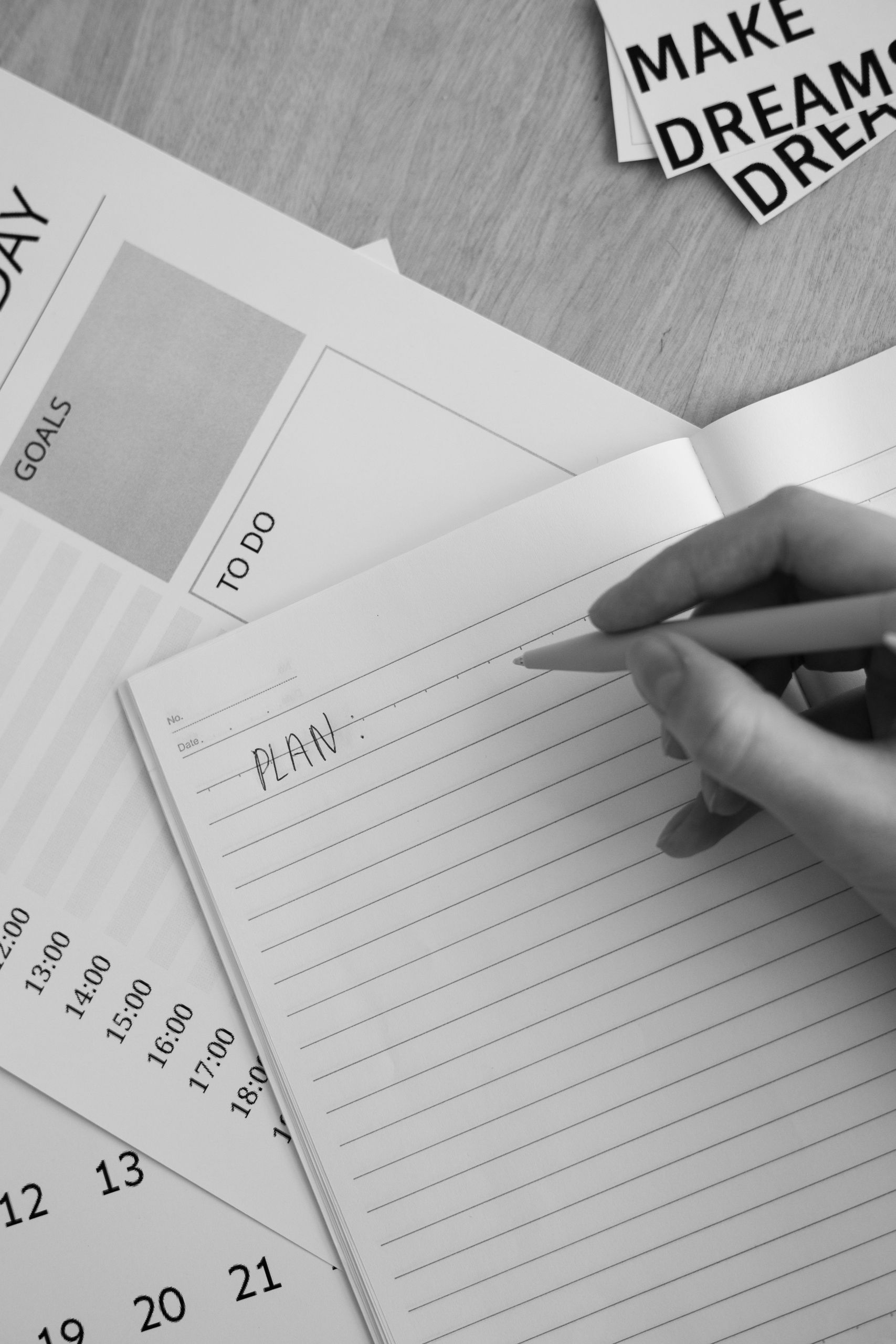 Hand writing 'plan' in a notebook next to a to-do list and weekly calendar, black and white photo representing soft planning